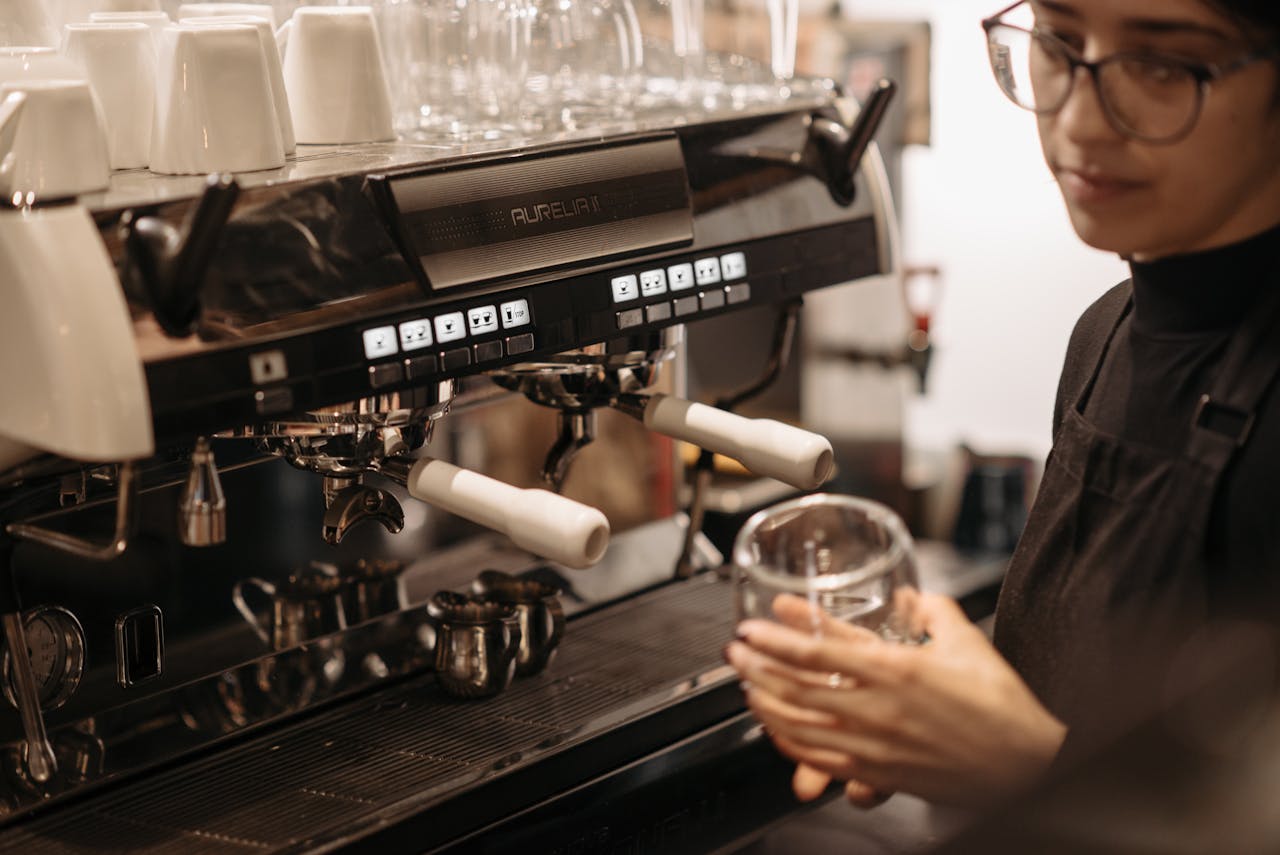 Barista in black apron making coffee with espresso machine at a cozy cafe.
