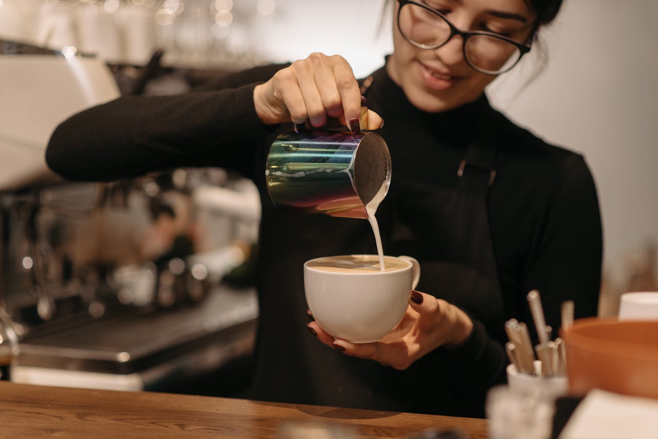 Young female barista creating coffee art by pouring milk at a cafe.
